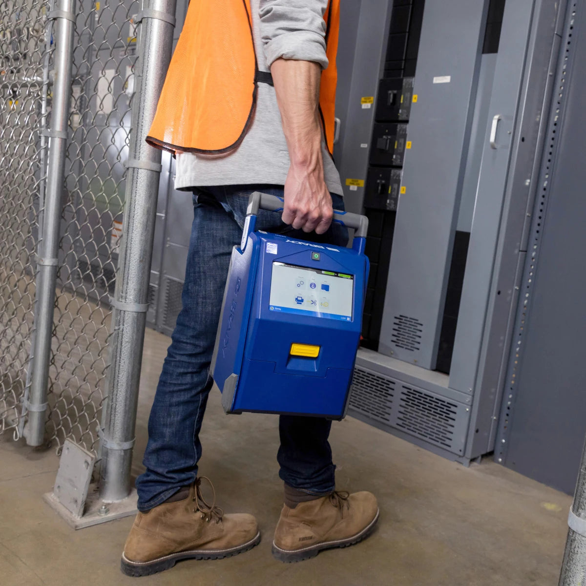 Worker carrying the battery-powered Brady i4311 by its handle through an industrial facility