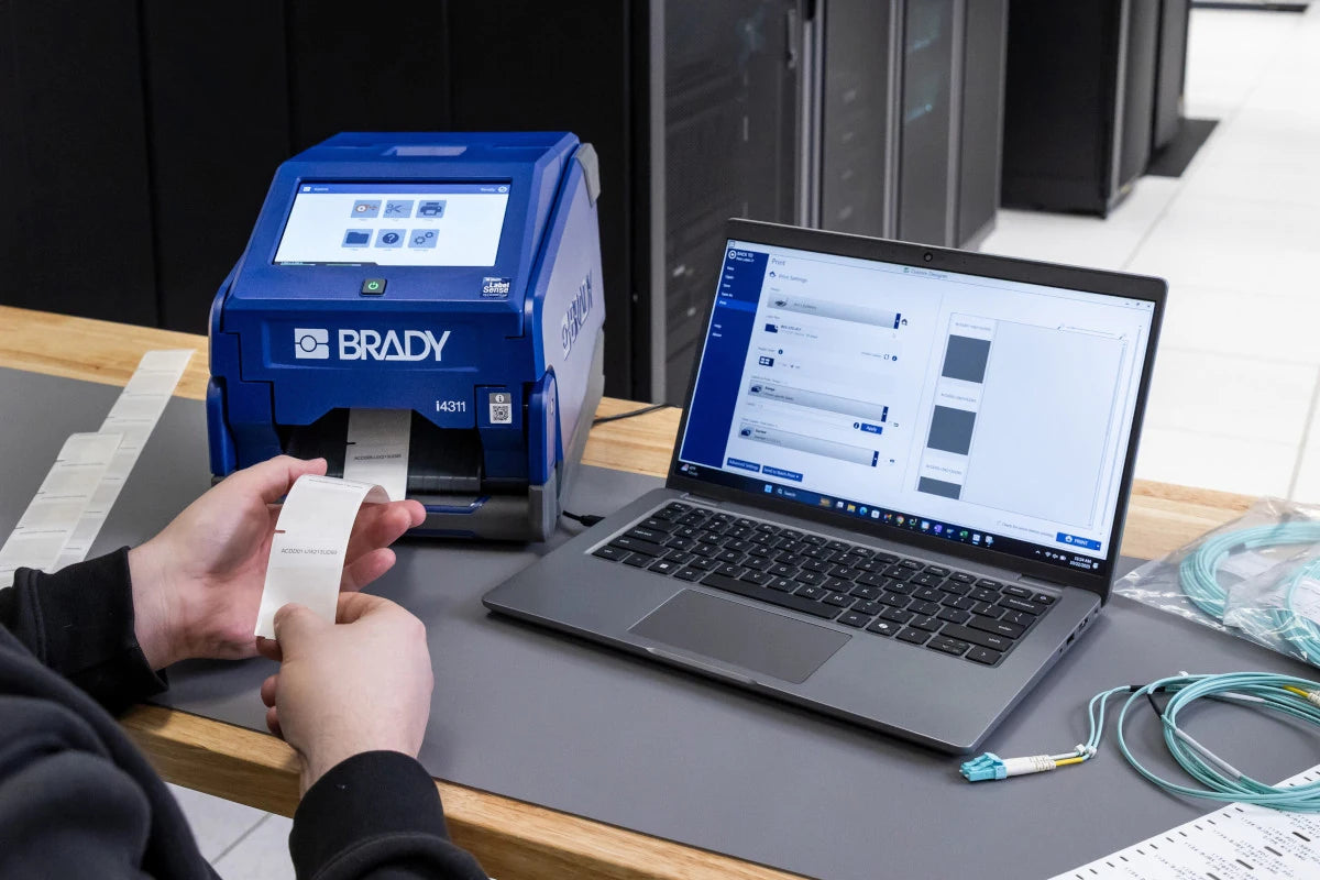Creating labels on a laptop beside the Brady i4311 in a datacom workspace