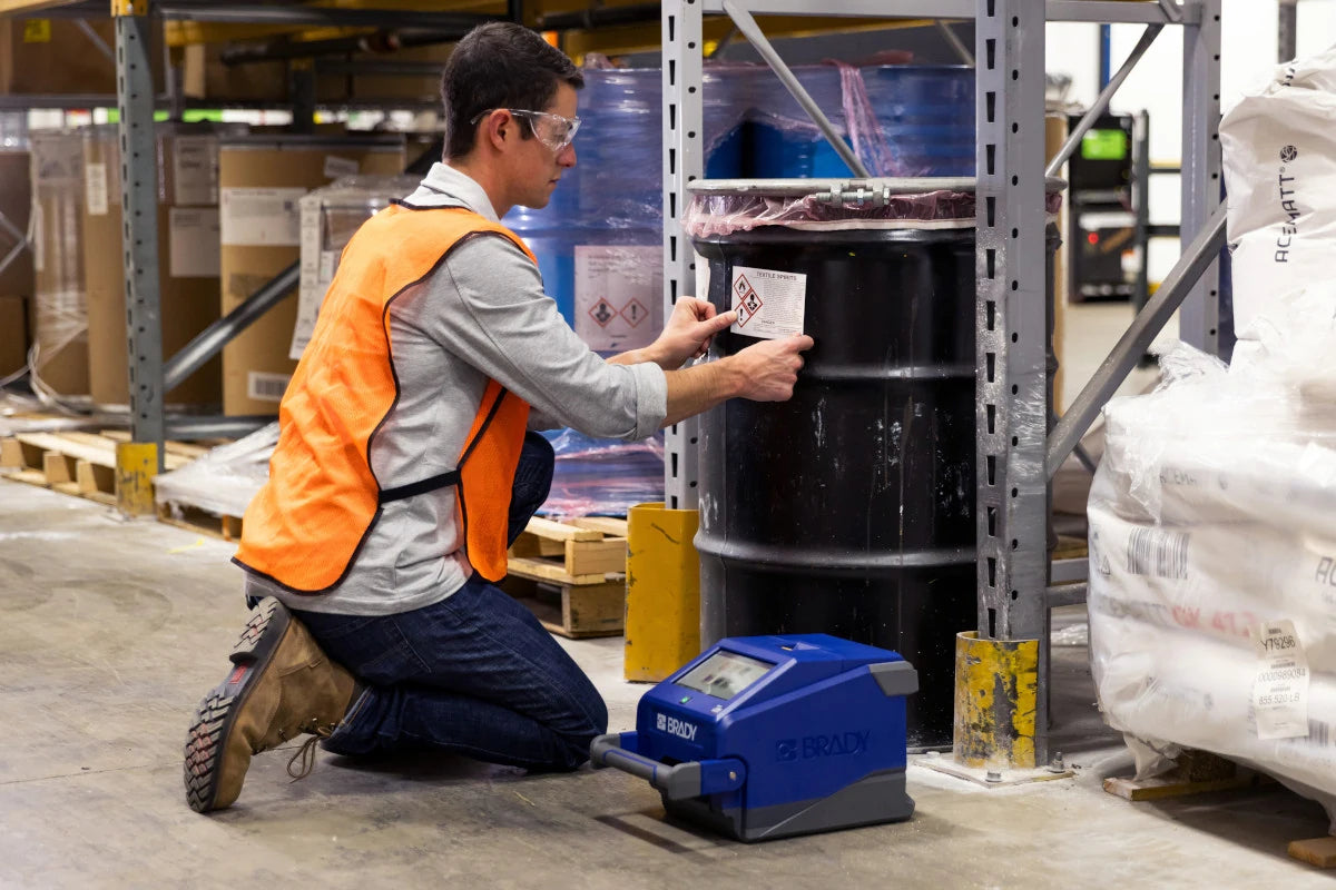 Worker applying a label to a storage drum in a warehouse